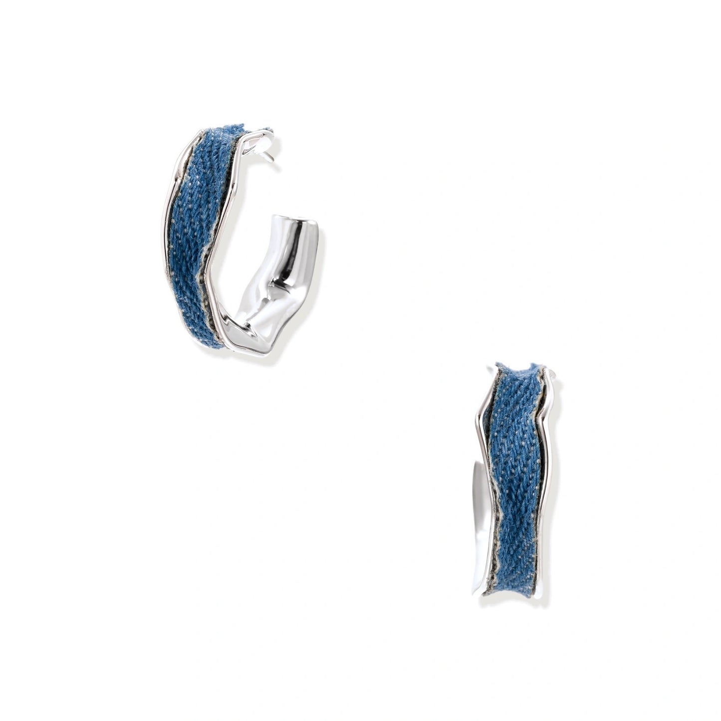 Silver huggie hoops with blue denim fabric inlay strip and polished white gold plated finish on cream background.