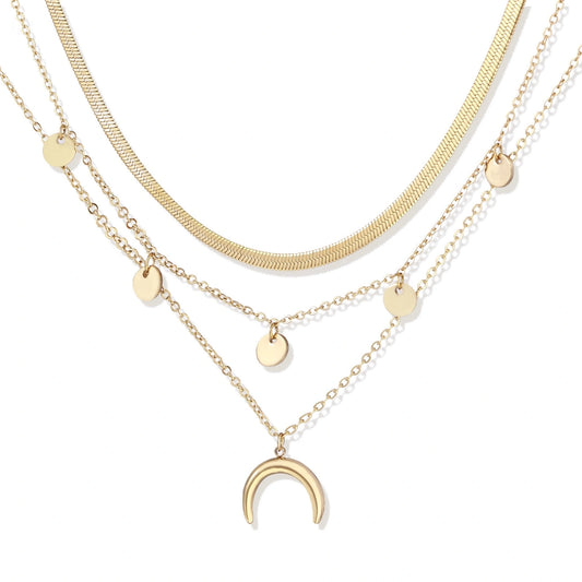 Four-layer gold necklace with herringbone chain, disc charms, and crescent moon pendant on cream background
