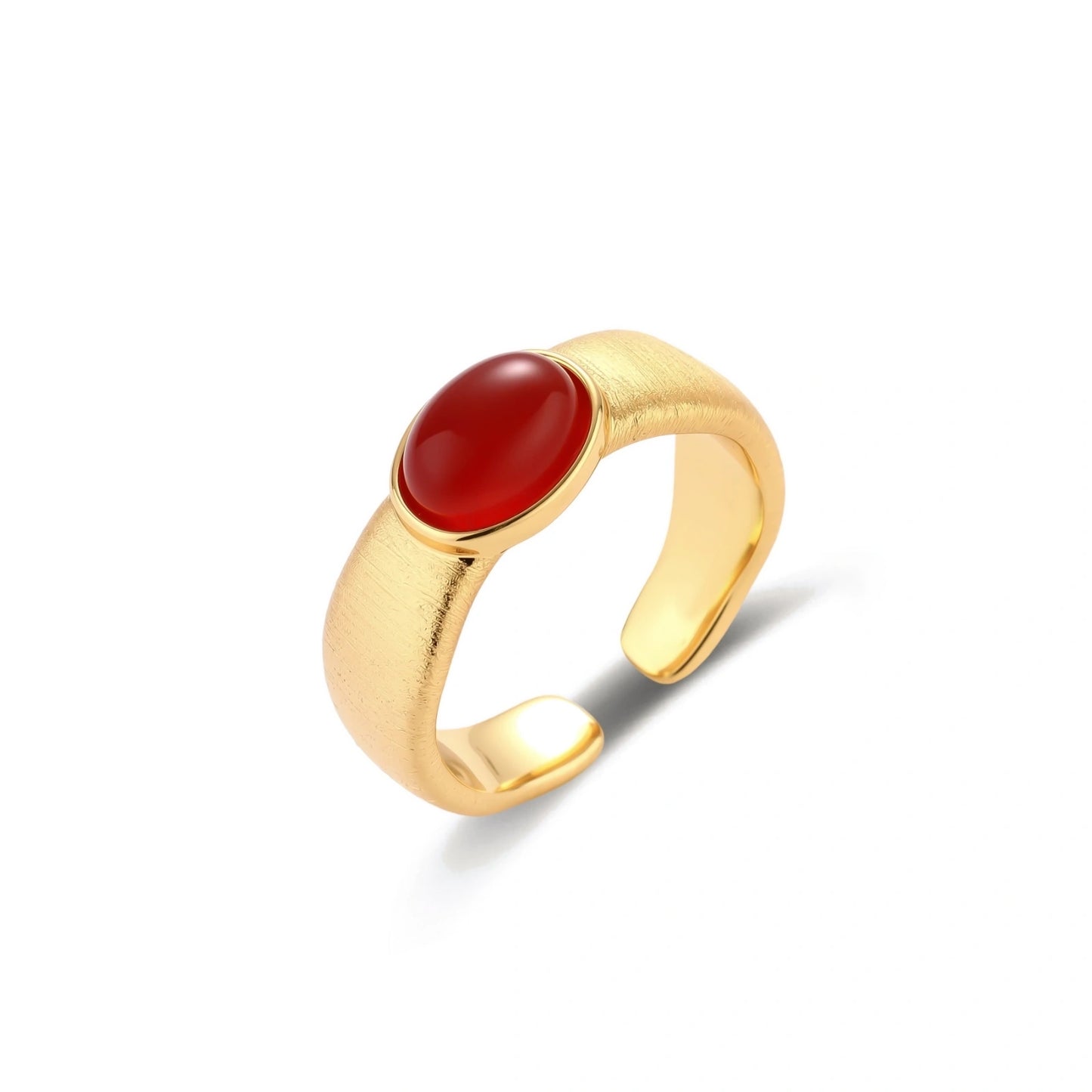 Close-up of brushed gold-plated ring with deep red oval stone, featuring adjustable band design on neutral background.